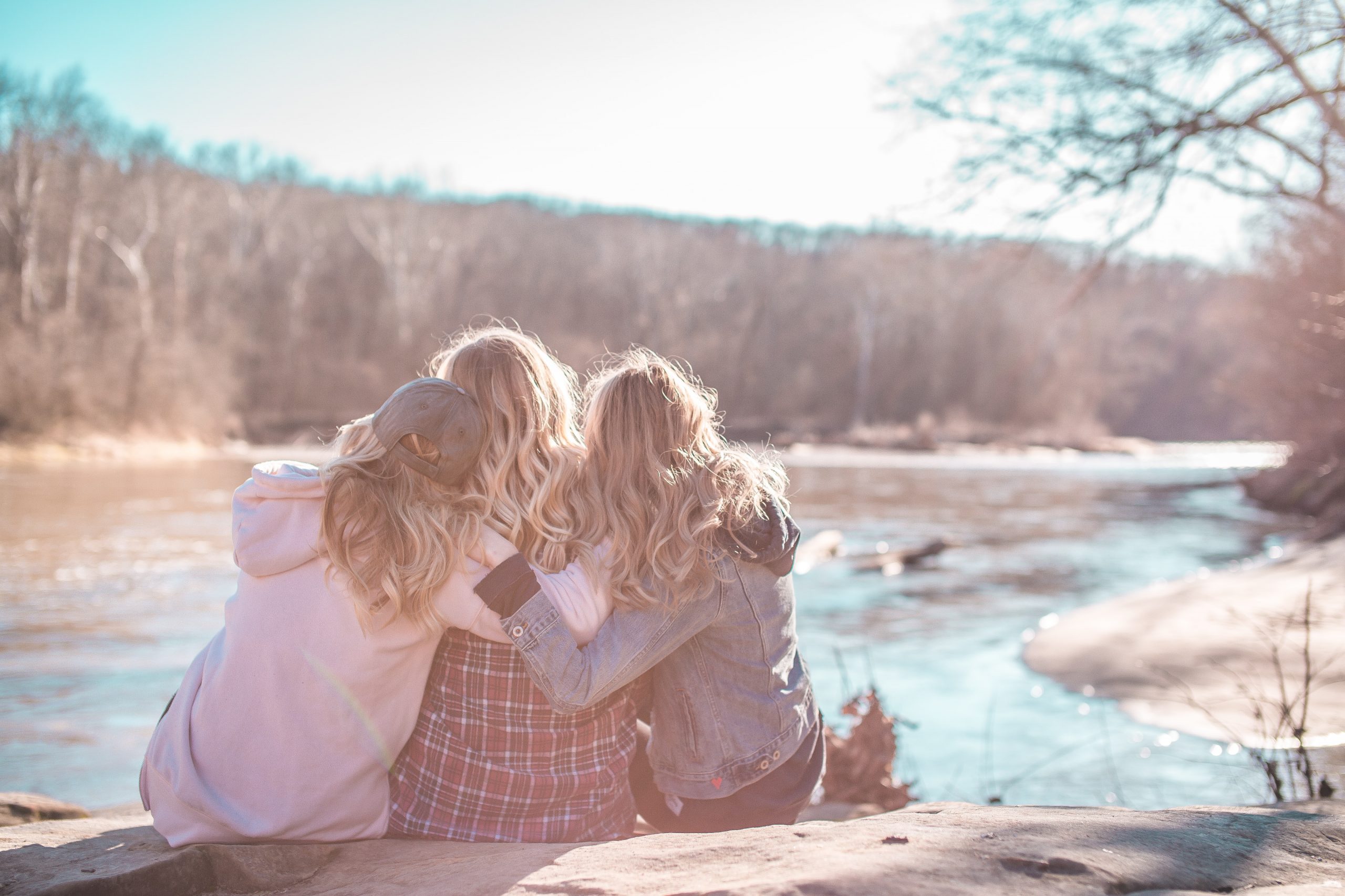 Three women in a supportive embrace looking away.